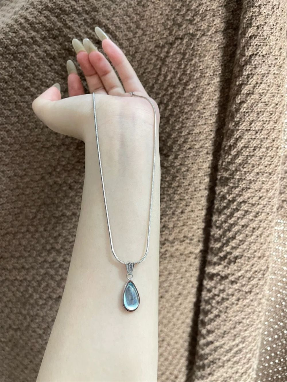 DewLume blue pendant necklace with its silver-tone chain extended over a cream sleeve