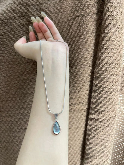 DewLume blue pendant necklace with its silver-tone chain extended over a cream sleeve