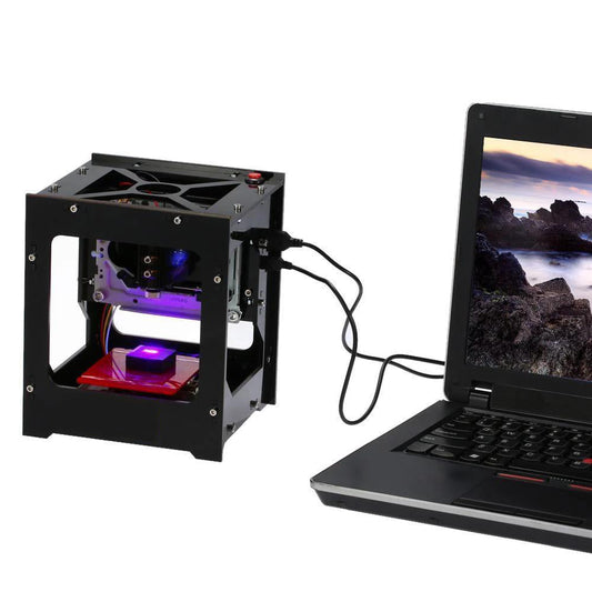 Small laser engraving machine next to a laptop on a white background