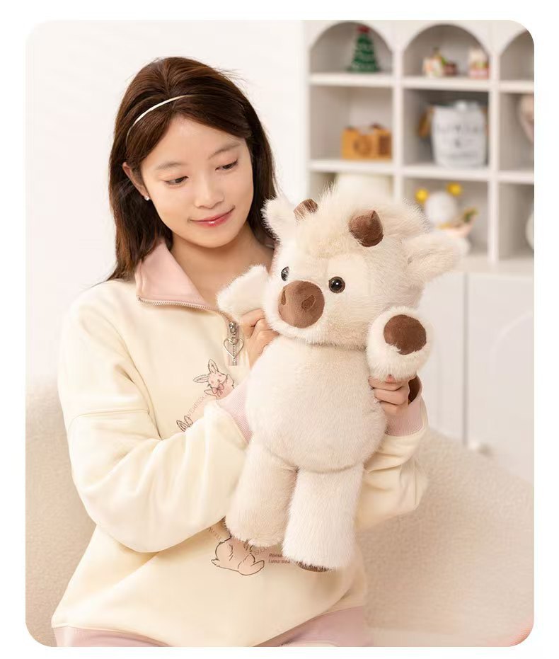 CreamCuddle cream Highland cow plush held by a seated person to show its size